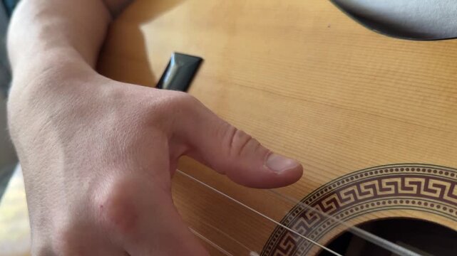 Close-up of a man playing an acoustic guitar. The frame shows the fretboard and the musician's hand
