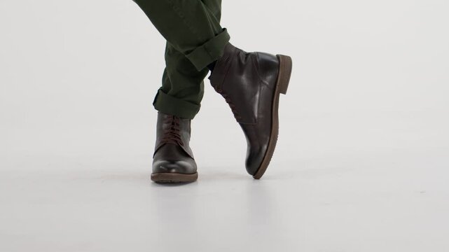 Male dancer performing a step in brown leather boots and green pants isolated on a white background