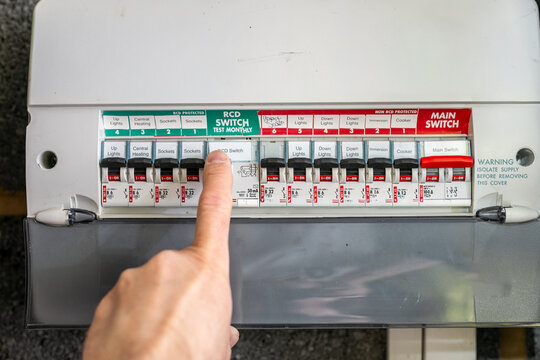 Person flicking a switch on a UK consumer unit, also known as a fuse box or distribution board, inside a residential property. The image represents household electrical control, power management
