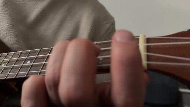 Man pressing strings on ukulele fretboard close up at home, playing chord, music practice moment, creative hobby activity, musical performance