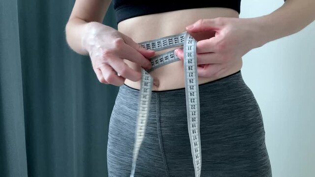 A woman measures her waist using a measuring tape. The problem of excess weight. Self-control and desire to improve physical condition and well-being