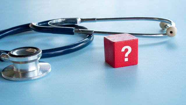 A red block with a white question mark standing next to a medical stethoscope on a blue background symbolizing medical uncertainty