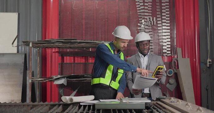 Sales engineer meets a client in an industrial workshop, reviewing quotation details, discussing costs and capabilities, and negotiating terms for a custom production project.
