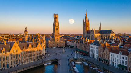 Obraz premium Panoramic view of Bruges city center with Belfry tower and Basilica of the Holy Blood under a full moon.