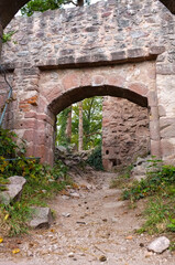 Fototapeta premium Interior view of a medieval stone archway at Haut-Ribeaupierre castle ruins. Historic fortification with pink sandstone walls and a forest path in Ribeauville, Alsace, France