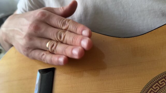 Person hitting acoustic guitar body with palm close up at home, producing strong rhythmic percussion sound, improvised music activity, creative hobby concept