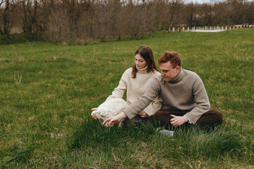 Fototapeta premium Lifestyle scene of a couple outdoors on a grassy field, smiling as they cradle a playful goat kid, cozy sweaters, natural light, gentle breeze, calm countryside atmosphere