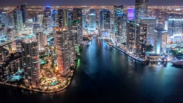 Night hyperlapse of a metropolitan city downtown with illuminated skyscrapers by the water. Aerial time lapse view of urban waterfront architecture and financial district.