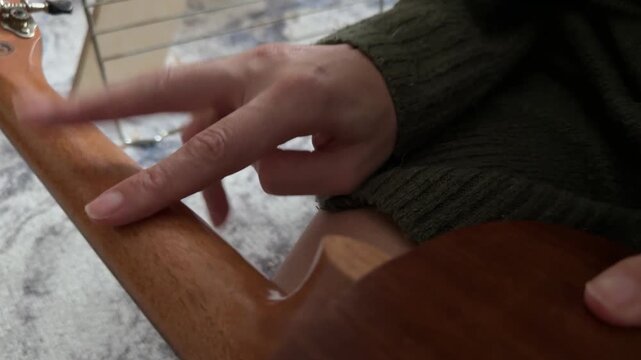 Person tapping fingers rhythmically on ukulele neck close up at home, producing soft percussion sound, improvised music activity, creative hobby concept