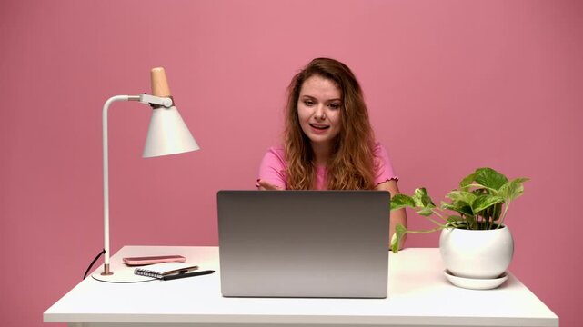 Young woman showing different emotions during a video call on her laptop against a pink background