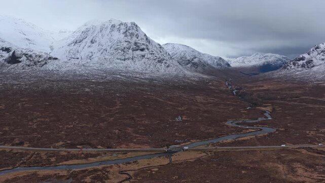 Scenic aerial view of the river etive bridge and road, with cars driving through the glencoe valley beneath snowy mountains