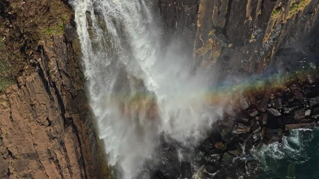The majestic mealt falls cascading down the rugged kilt rock cliffs on the isle of skye, with a beautiful rainbow forming in the mist