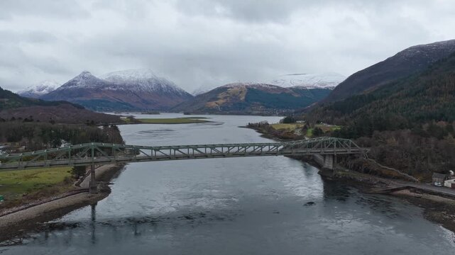 Aerial view of the historic ballachulish bridge crossing loch leven. Majestic snow capped mountains and a cloudy sky in the background