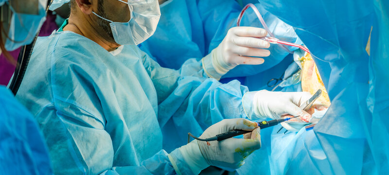 Concentrated surgical team of professional doctors performing complex surgery using specialized medical instruments in a sterile operating theater.