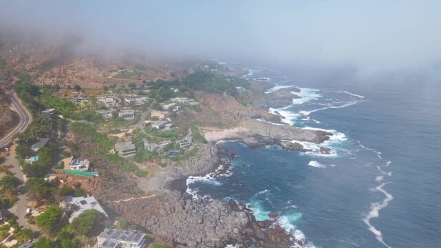 Aerial orbit of the Punta Pite coastline, with luxury mansions perched atop rocky mountains; Papudo, Chile, hidden among the clouds