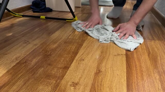 Man wiping wooden floor with cloth at home, cleaning routine, hygiene maintenance, domestic work, household care