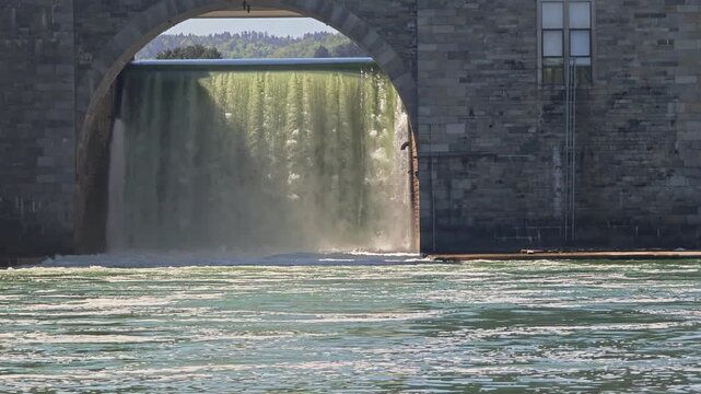 Powerful water dam overflow under a masonry archway on a sunny day