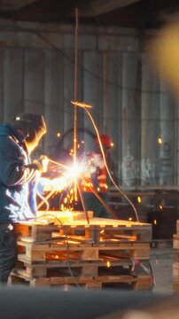 At the construction site, contractors weld metal using a resistance welding device, wearing full safety gear while coordinating precise teamwork in the busy industrial environment
