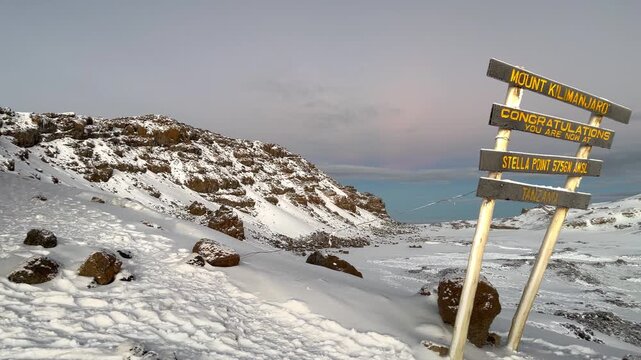 Breathtaking sunrise at Stella Point on the way to Kilimanjaro summit, Tanzania. Snowy mountain landscape with a congratulations sign at 5756 meters altitude. Extreme trekking. 4K