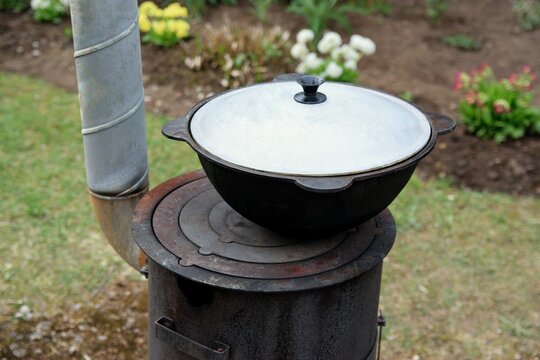 Traditional kazan with lid on a wood-burning stove in a blooming garden background