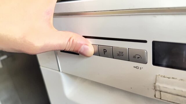 Close up of hand pressing button on dishwasher control panel, selecting washing program, modern kitchen appliance usage concept