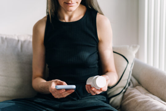 Woman takes prescription medication while using phone in a living room setting