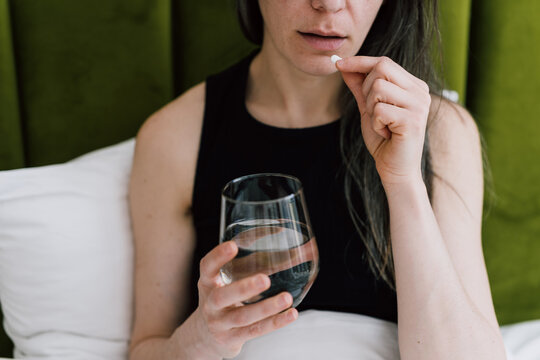 Woman takes a pill with water in her bedroom during morning routine