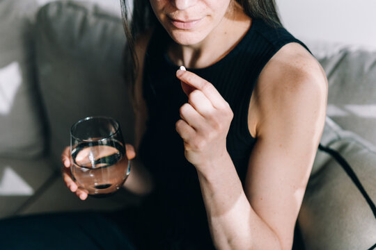 Woman takes prescription pill with water in a living room setting