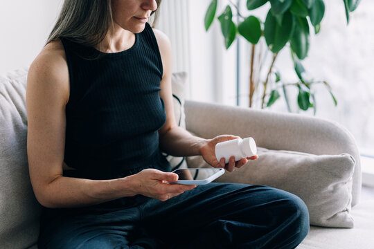 Woman taking a pill while using a phone in a living room