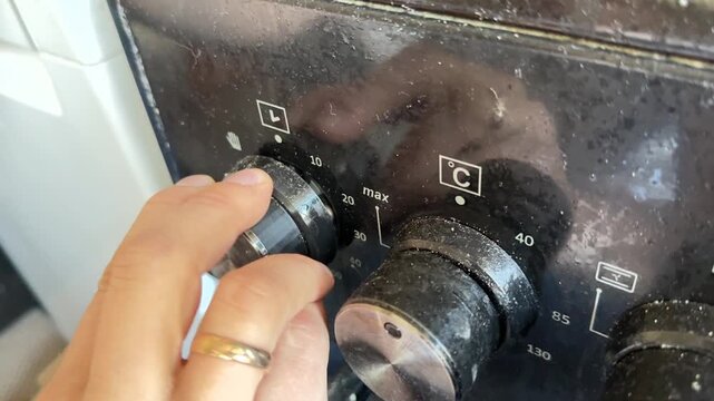 Close up of hand turning oven timer knob, setting cooking time on kitchen appliance, home cooking and kitchen control concept