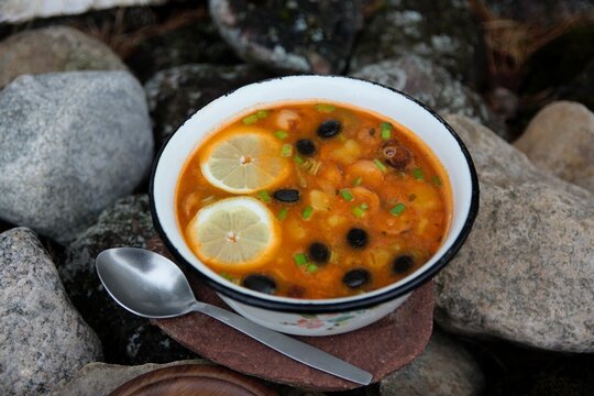Homemade traditional Eastern European solyanka soup in enamel bowl on natural stones background, side view, outdoor