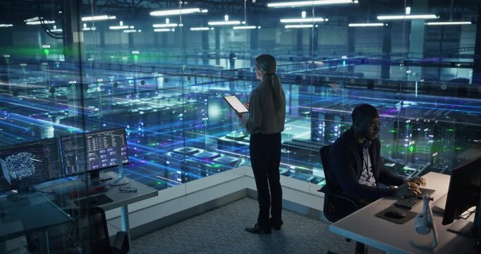 Male Specialist Works at a Computer While a Female Analyst Reviews a Tablet, Monitoring Information Flow Overlays That Map Network Traffic, System Status, and Data Center Activity.