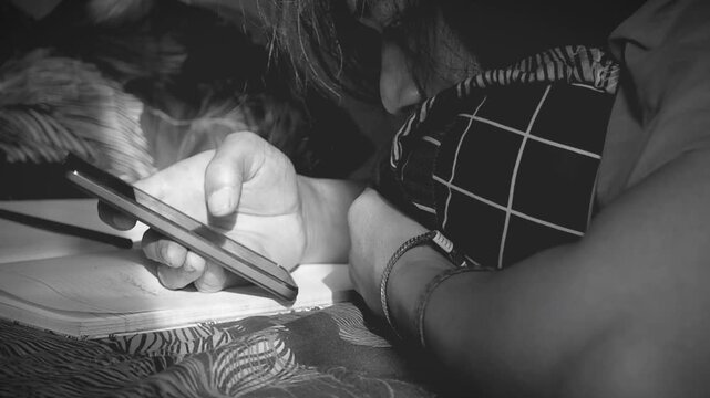 Person Lying Face Down Using Smartphone on Bed in Low Light Room