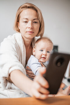 Authentic shot of neo mother and her newborn baby making a video call to father or relatives with laptop on a sofa in a living room.