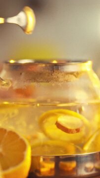 In a warm kitchen, a man crafts a tea blend by gently stirring sliced lemons and ginger in a teapot with a spoon, filling the air with a fragrant, invigorating aroma typical of tea-making