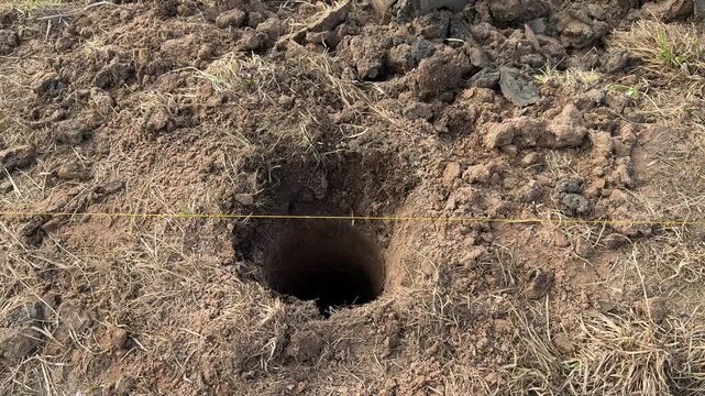 Deep round post holes yellow string preparation for concrete pouring with supports, even spacing across compacted soil, top down