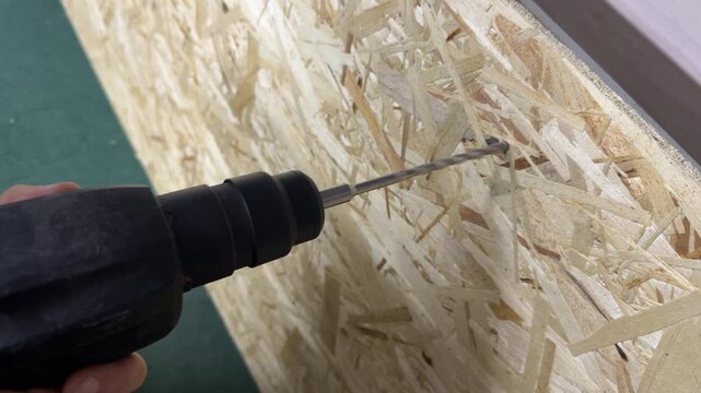 Electric drill driving screw into OSB wood board, home improvement and construction work concept