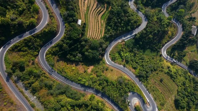 Top-down drone view of winding road in Ha Giang, Vietnam. Serpentine mountain route crossing green hills and terraced landscape with scenic curves from above.