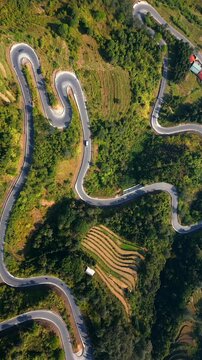 Top-down drone view of winding road in Ha Giang, Vietnam. Serpentine mountain route crossing green hills and terraced landscape with scenic curves from above.