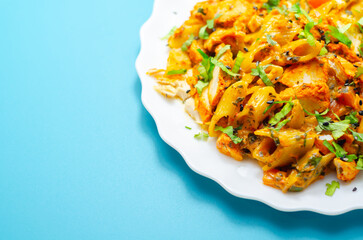 Bright orange pasta dish with chicken and herbs on white plate © Q77photo