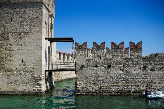 View of the historic Scaligero Castle with its stone walls and drawbridge over the turquoise water of Lake Garda in Sirmione, Lombardy, Italy.