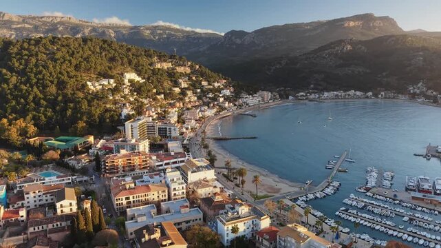 Yachts anchored in circular marina of Port de Soller, Mallorca, Spain. Aerial 4K: Green mountains enclose bay in Port de Soller, Mallorca, Spain. Waterfront buildings line beach in Soller, Spain