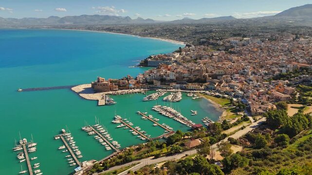 Aerial UHD view of ancient fortress on coast of Castellammare del Golfo, Sicily, Italy. Moored boats fill harbor of Castellammare del Golfo, Italy. Turquoise sea washes Castellammare del Golfo