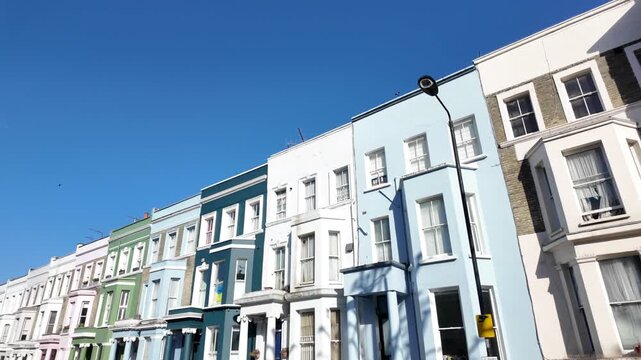 Low-angle perspective of colorful pastel houses and apartments on a beautiful sunny day in the portobello road area of notting hill, london, with a bright blue sky