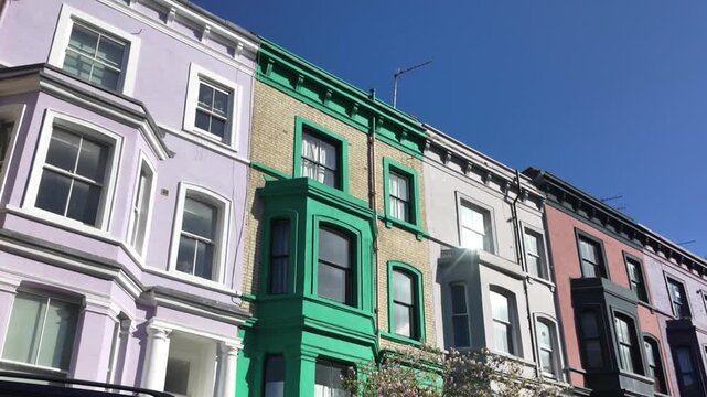 Colorful notting hill row houses showcasing their vibrant victorian architecture and charming bay windows against a clear blue sky, a famous london residential street