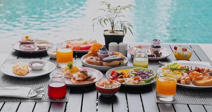 Breakfast spread with eggs benedict, pastries and fruit juice served on wooden table, poolside resort environment, outdoor morning dining for hospitality and travel marketing