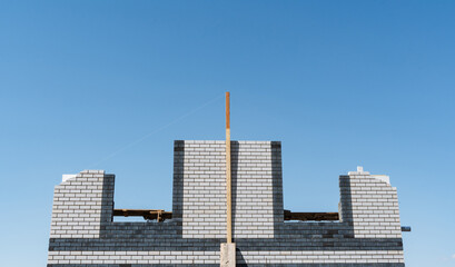 Obraz premium Unfinished Concrete Framework Stands Tall Against Bright Blue Background. Partially Completed Cinderblock Construction With Central Timber Support Visible Against Clear Sky