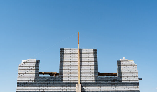 Unfinished Concrete Framework Stands Tall Against Bright Blue Background. Partially Completed Cinderblock Construction With Central Timber Support Visible Against Clear Sky