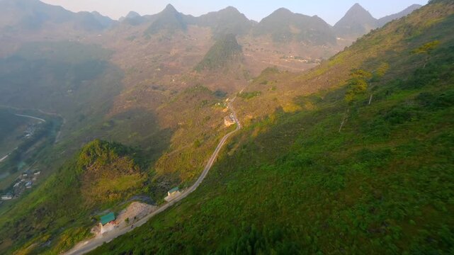 Cinematic FPV drone flight above winding mountain road in Ha Giang, Vietnam. Aerial movement through green valleys and rugged peaks in northern Vietnam landscape.