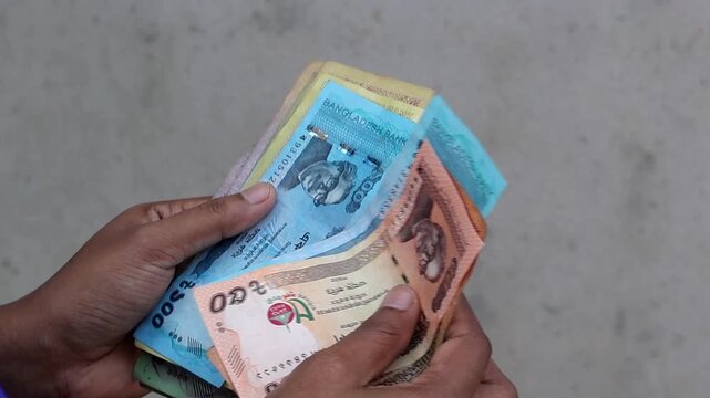 Close-up of a person's hands counting a stack of Bangladeshi Taka banknotes against a neutral background. This action represents financial transactions, savings, and the local economy in Bangladesh.